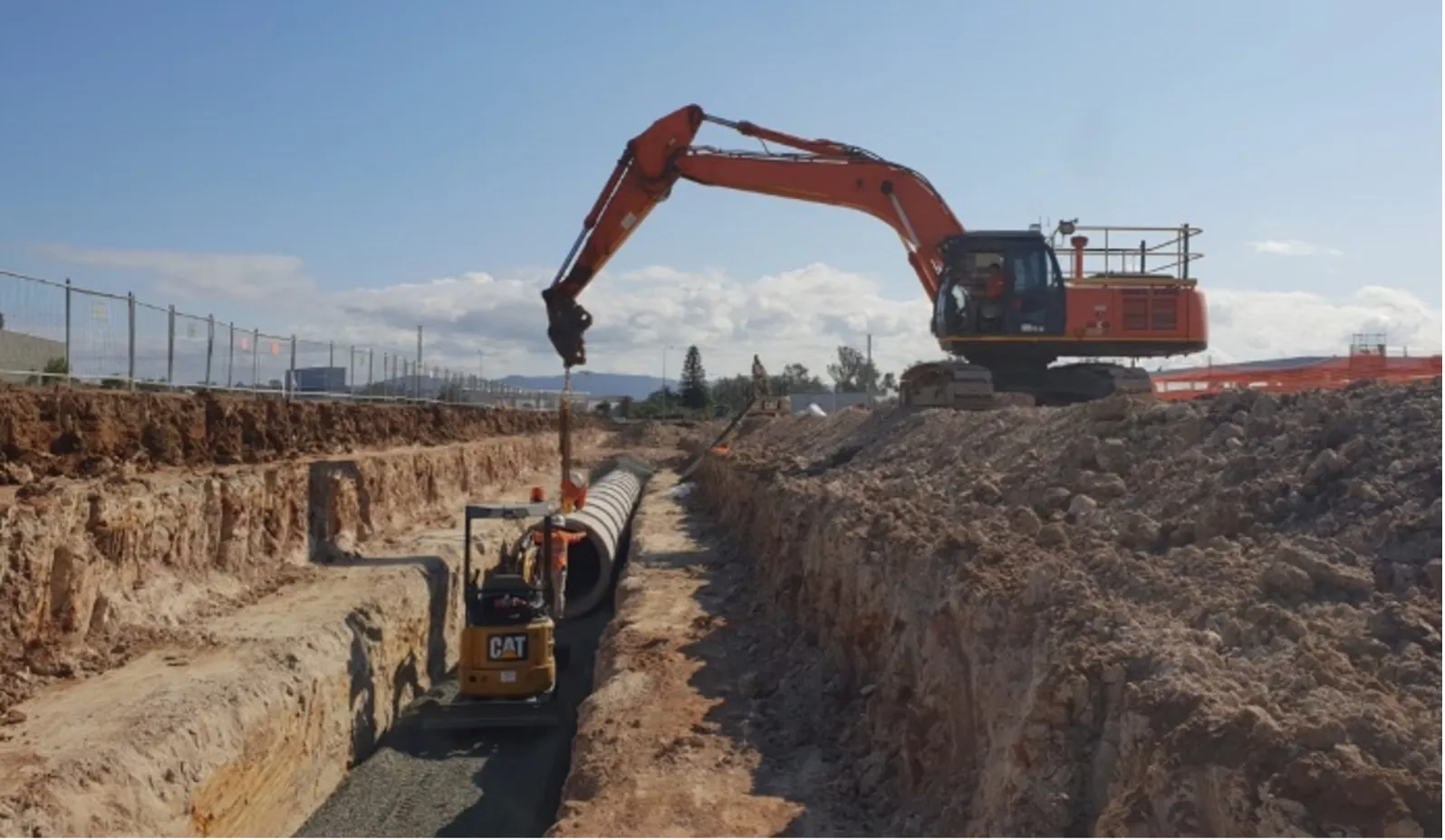 An orange excavator placing large pipes for the Costco Drainage Project